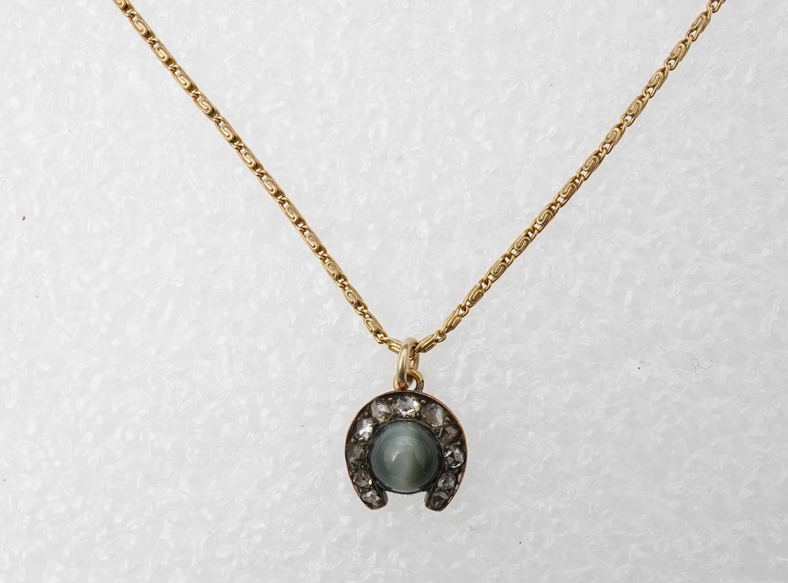 A yellow metal, cat's eye quartz and rose cut diamond cluster set horseshoe pendent, 11mm, together with a 9ct gold chain, 41cm, gross weight 5 grams.